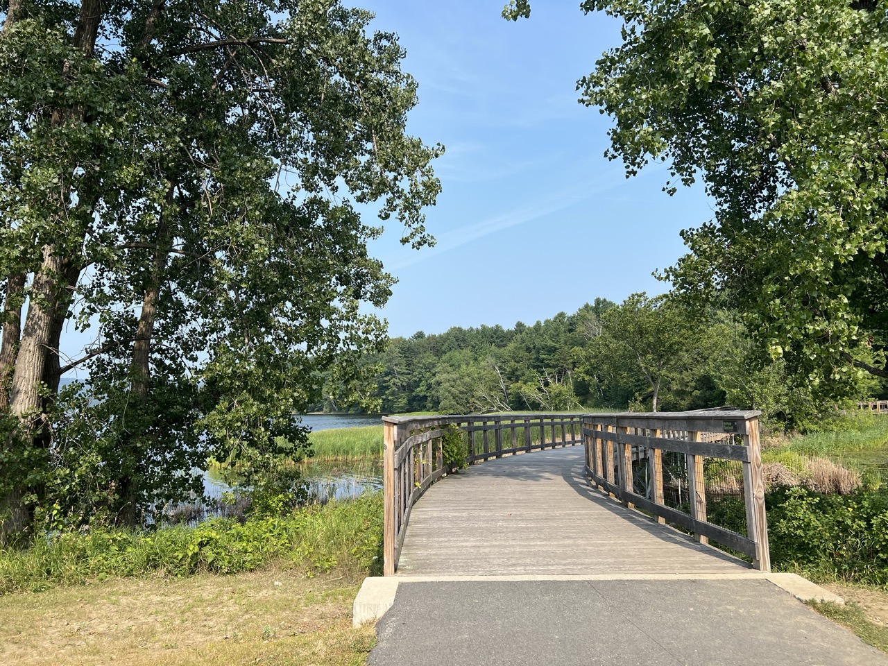 Curving boardwalk bridge over a bulrush wetland with views of Lake Memphremagog.