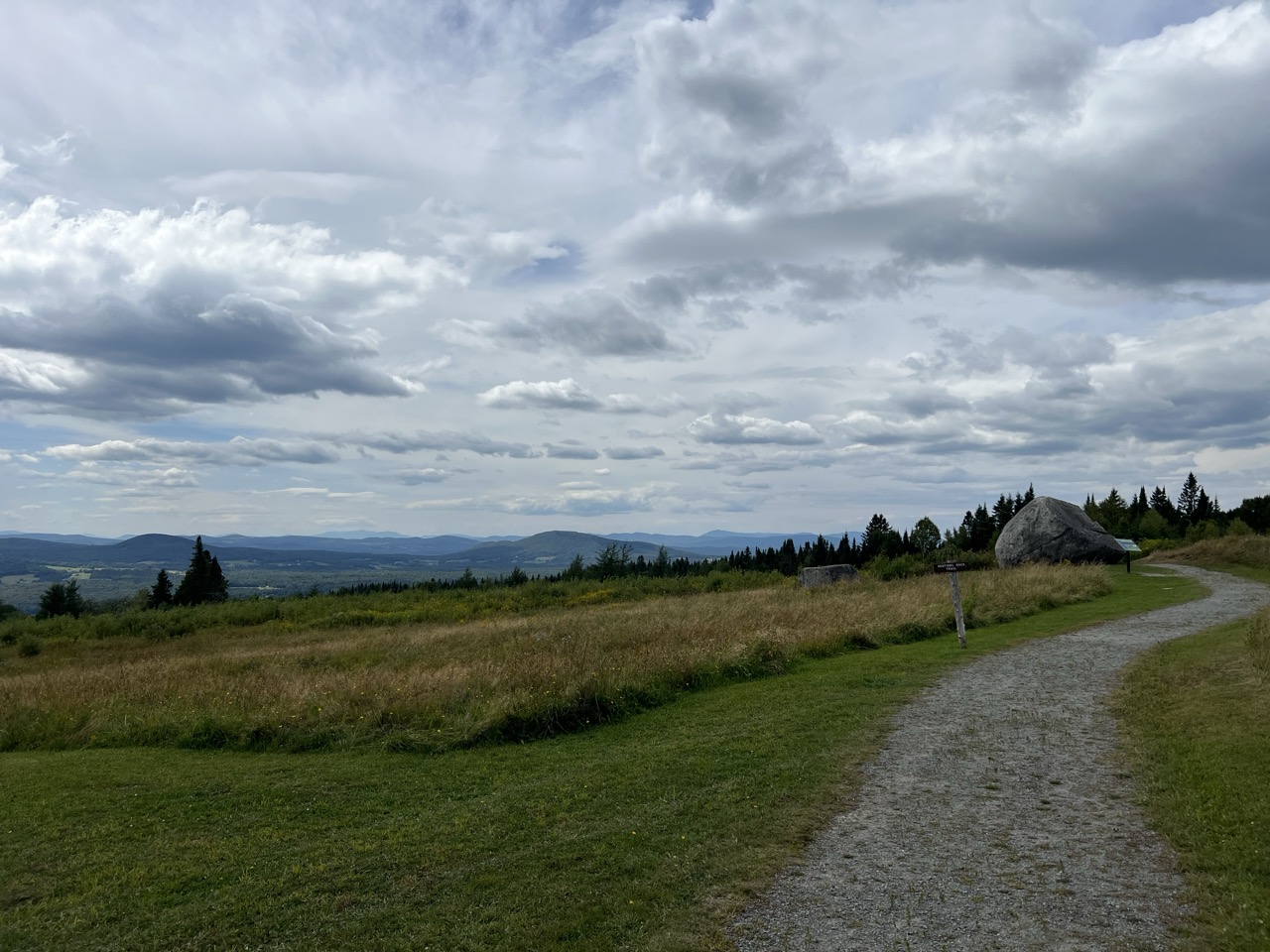 Winding path leading up to large boulder and dramatic views of distant mountains.